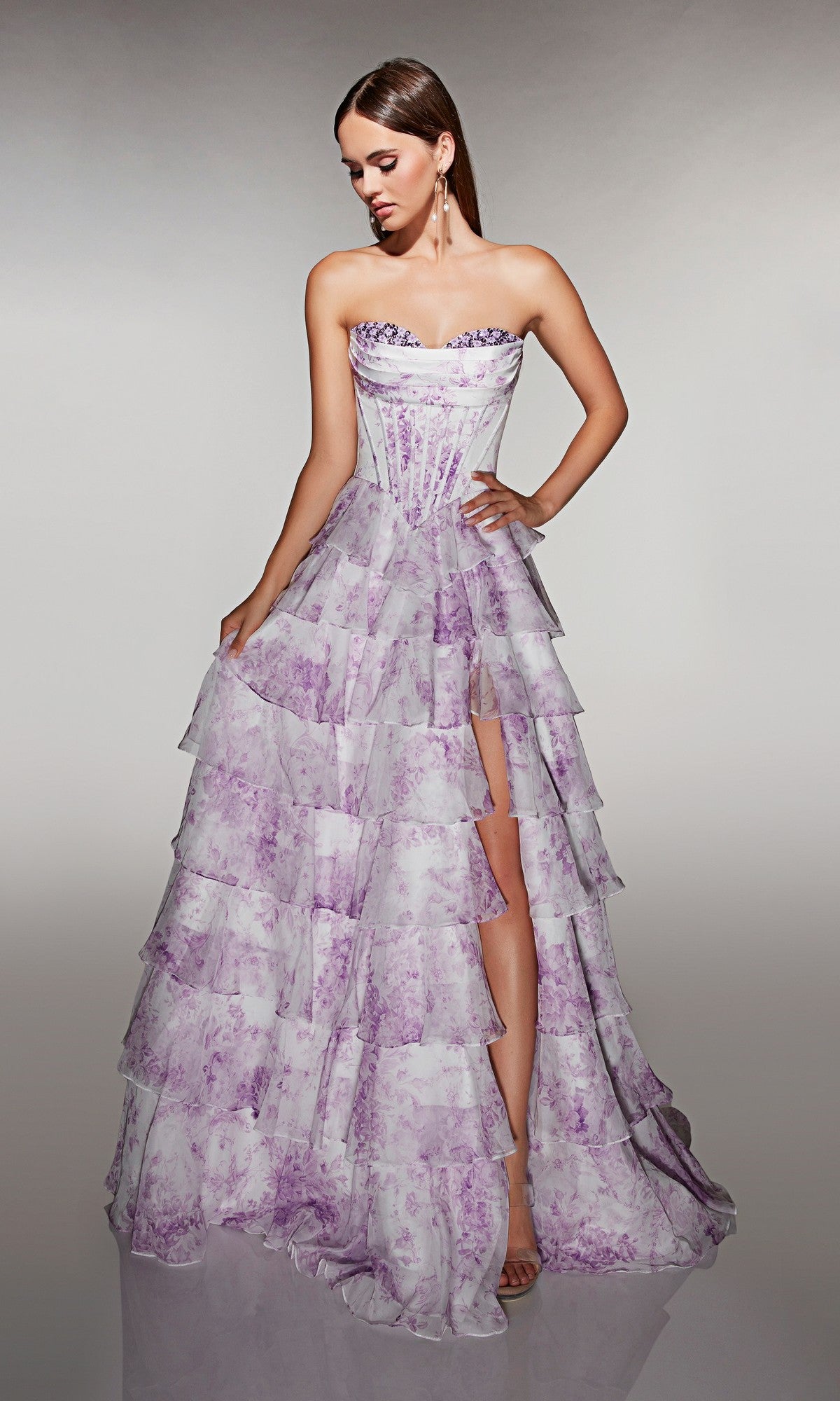 A woman in the Alyce 62192 long prom dress, featuring a strapless corset bodice and floor-length, tiered bright purple and white chiffon ruffle skirt with a high slit, stands against a plain background.